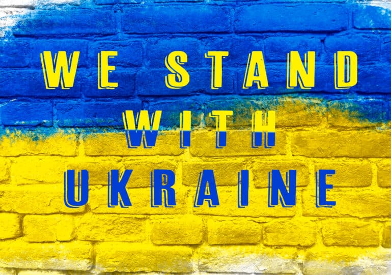 A bold message reading “We Stand With Ukraine” painted on a brick wall in blue and yellow, representing youth resilience, solidarity, and global leadership.